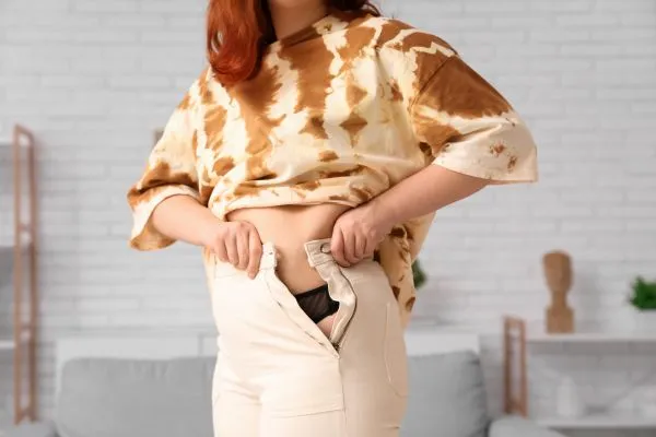 Image of woman trying to do her trousers up after pregnancy weight gain Sighthill